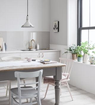 A grey kitchen with metallic silver pendant light over dining table with wooden chairs and black framed window with potted plants on windowsill