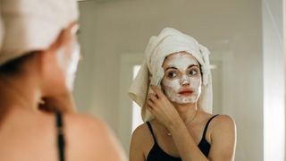 Woman with her hair wrapped in a towel applying a face mask at home