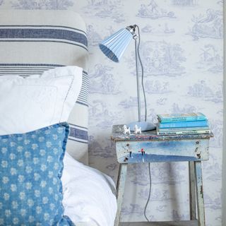 vintage bedside with weathered paint, blue lamp in front of toile du jouy wallpaper