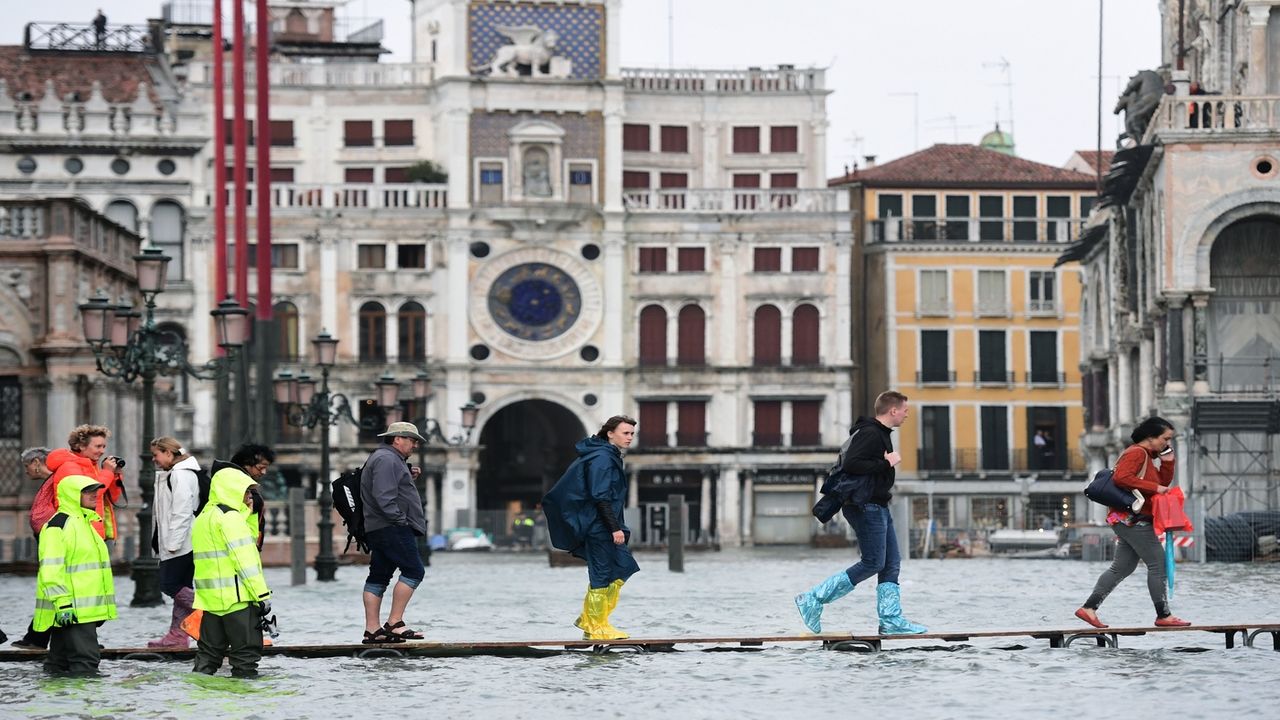 People walk on a footbridge in the flooded St. Mark's Square during a high-water (Acqua Alta) alert in Venice on October 29, 2018. - The flooding, caused by a convergence of high tides and a