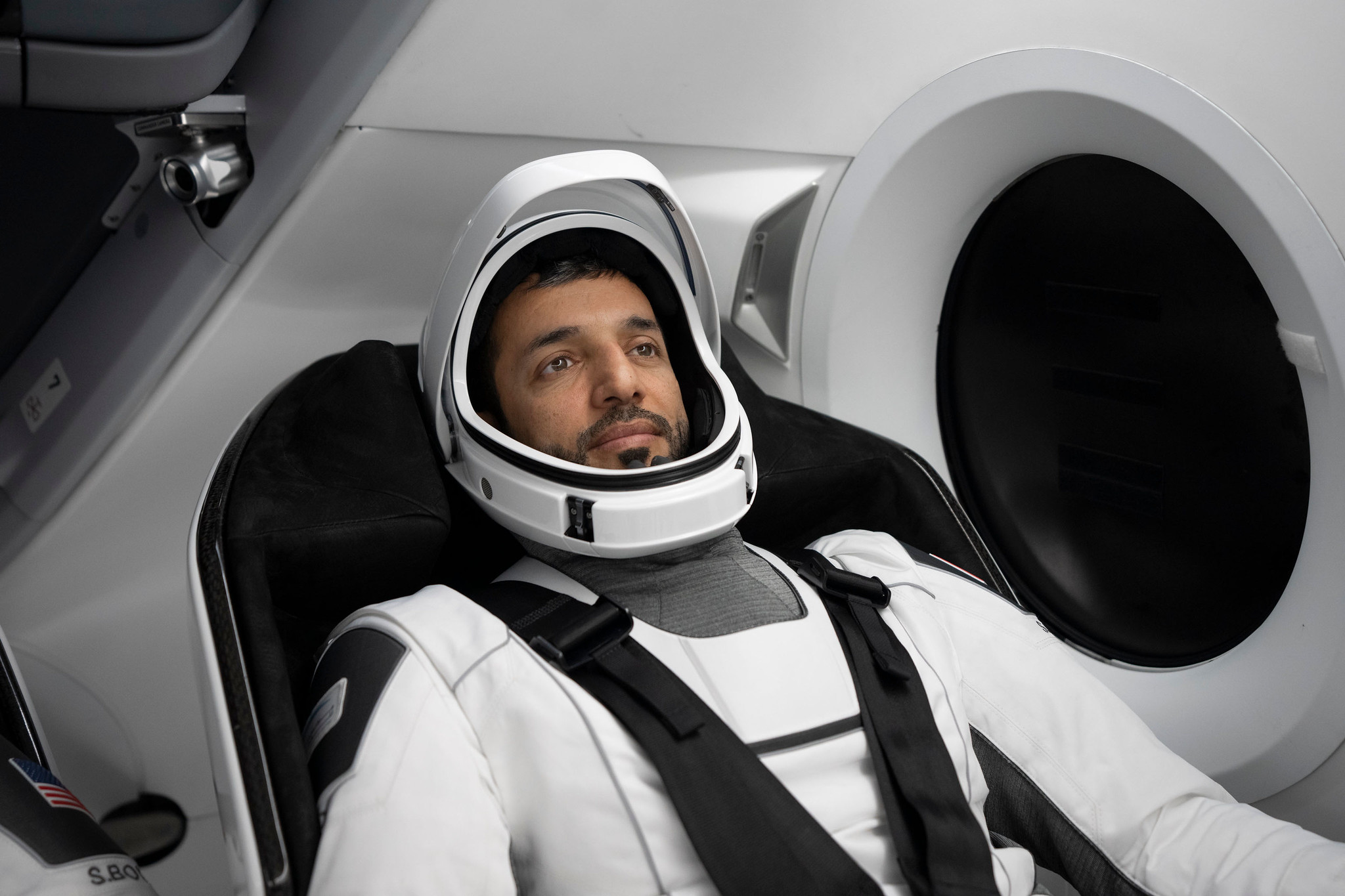 United Arab Emirates astronaut Sultan Al-Neyadi sitting in a spacecraft with seatbelt on, beside a round window