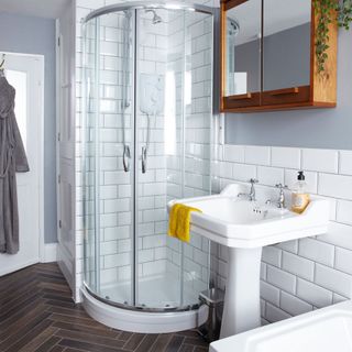 bathroom with wooden cabinet on grey paint and while tiles wall and shower area with white wash basin