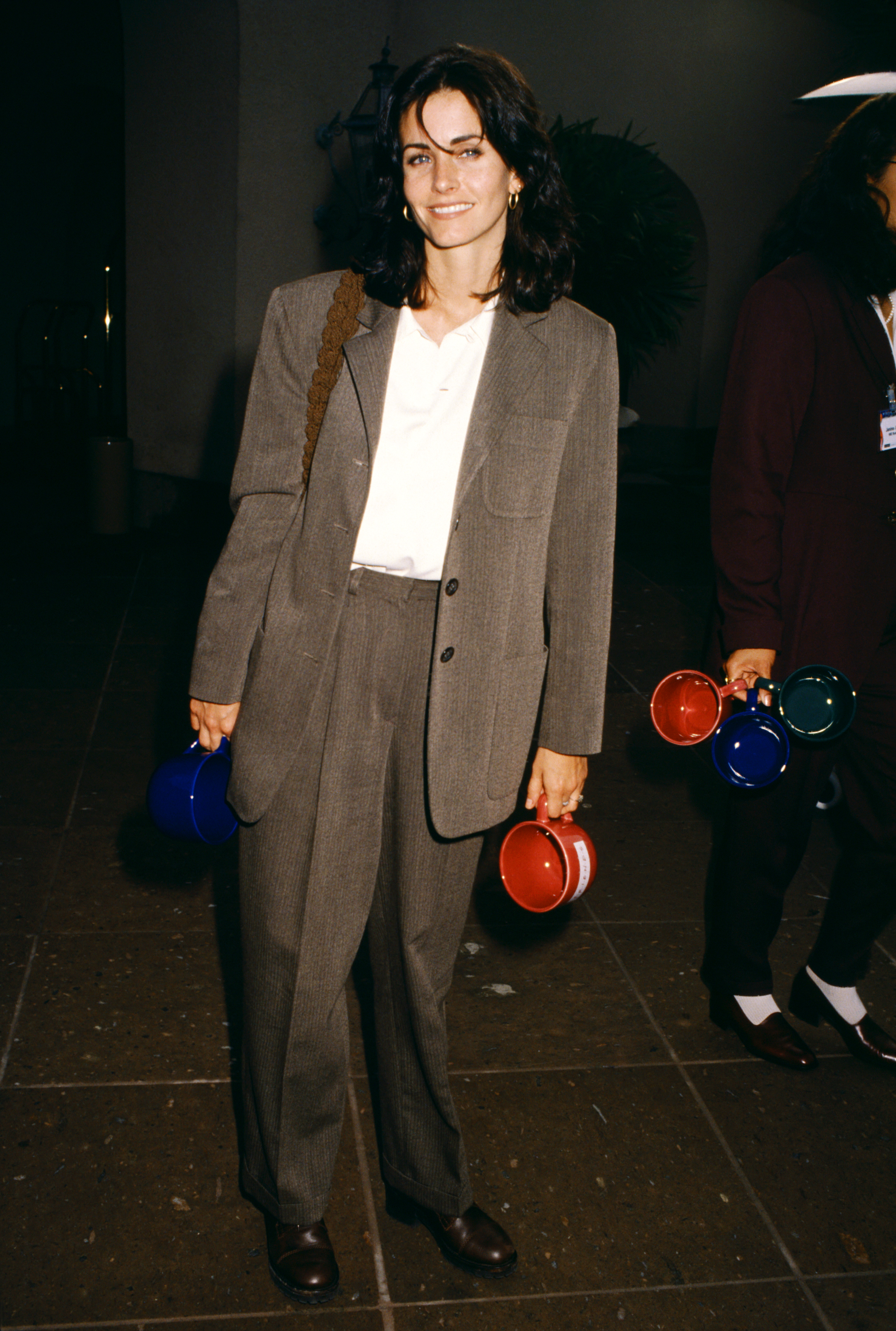 An image of Courteney Cox wearing a white shirt, a brown blazer and matching suit pants in 1995.