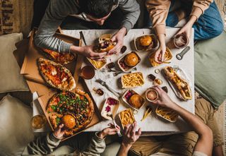 fast food dinner from delivery service. Flat-lay of friends eating burgers, fries, sandwiches, pizza, salad and drinking beer at quarantine home party over table background, top view