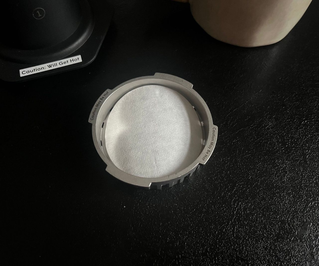 A paper filter in the cap of a stainless steel AeroPress on a black kitchen counter.
