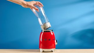 Smeg Personal Blender in the red colorways photographed in front of a blue background.