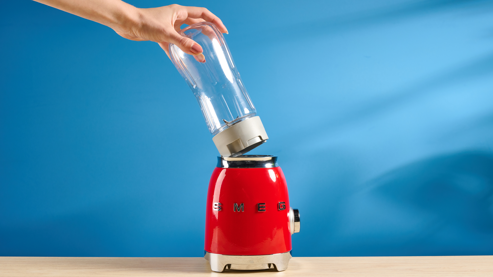 Smeg Personal Blender in the red colorways photographed in front of a blue background.