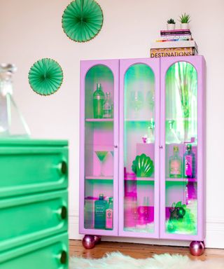 Bright purple drinks cabinet, bright green accents, wall decorations and furniture, shaggy rug on wooden floor