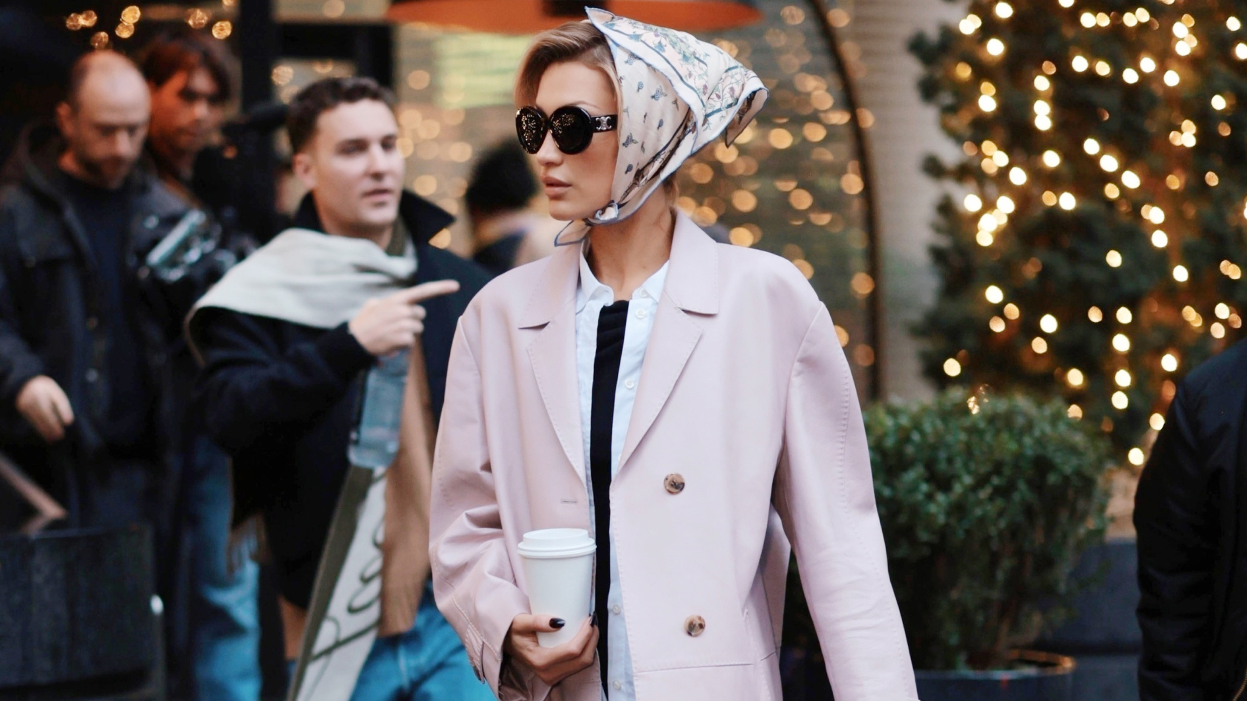 Bella Hadid wears a head scarf, pink coat, black capri pants, and black ballet flats.