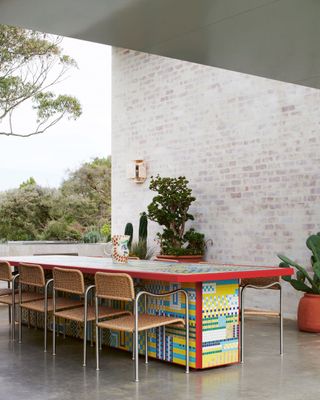 a modern dining room with indoor-outdoor connection, and large mosaic tiled table with rattan chairs, polished concrete floor, and limestone brick wall