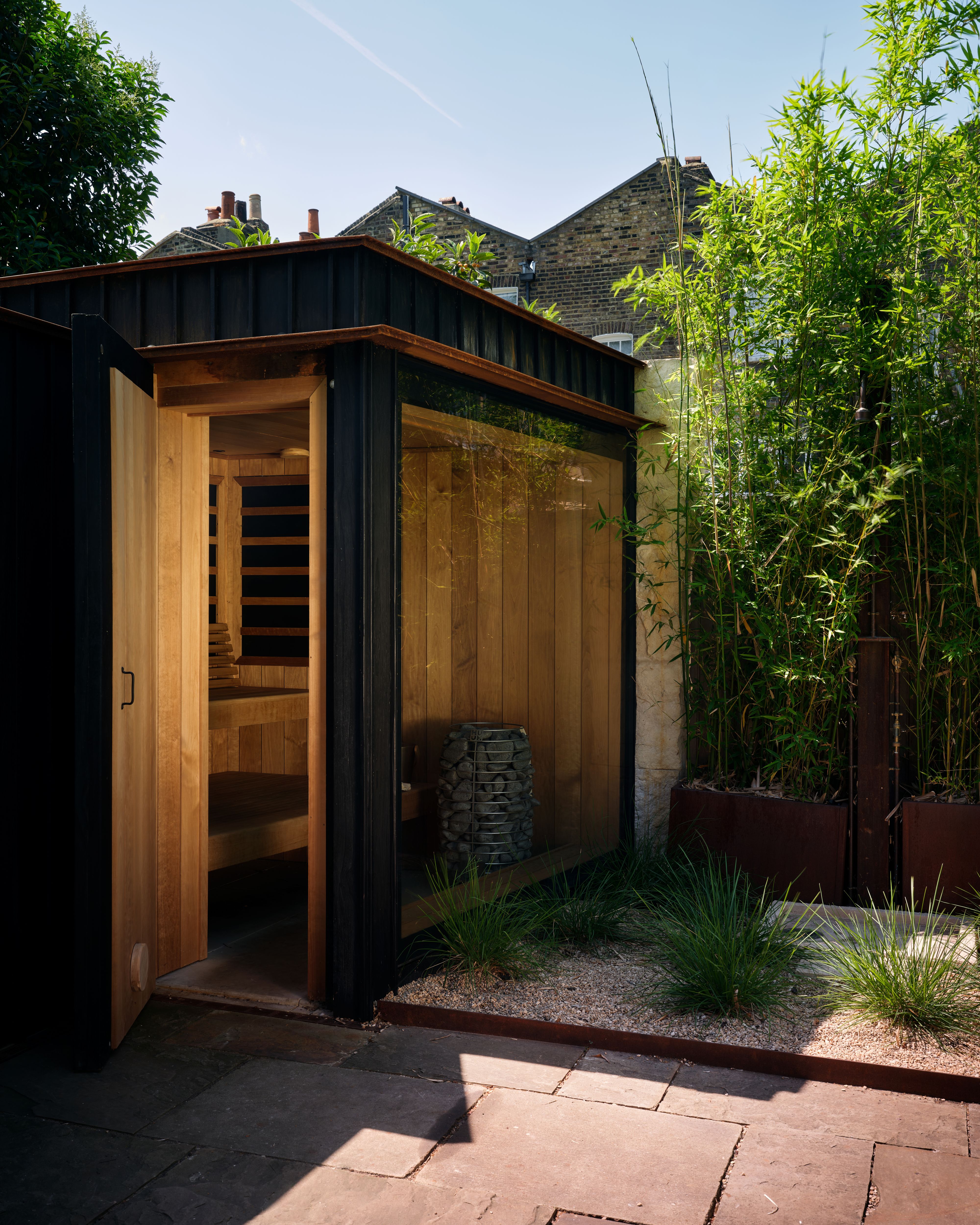 A wooden sauna with black exterior in a paved London garden