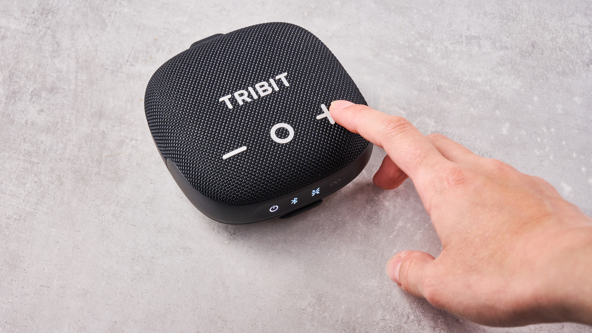 A woman's hand pressing the volume up button on the front of the Tribit Stormbox Micro 3.