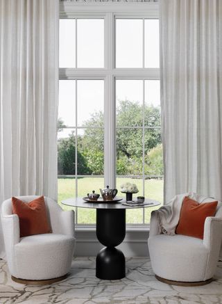 two white boucle chairs with a black coffee table in front of windows