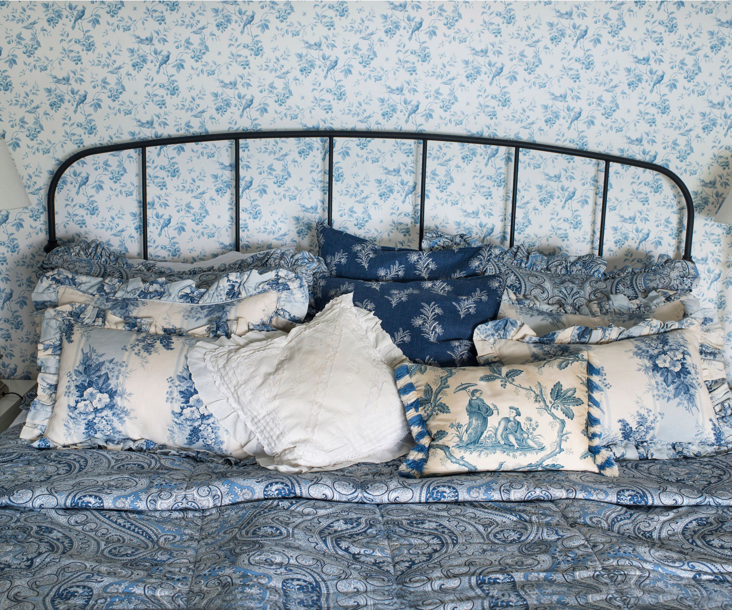 black cast iron bed with blue floral bedding and wallpaper