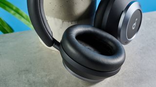 the soundcore space one pro headphones; a photograph of a pair of black over-ear headphones with cushioned cups and a soft headband, photographed in front of a blue background