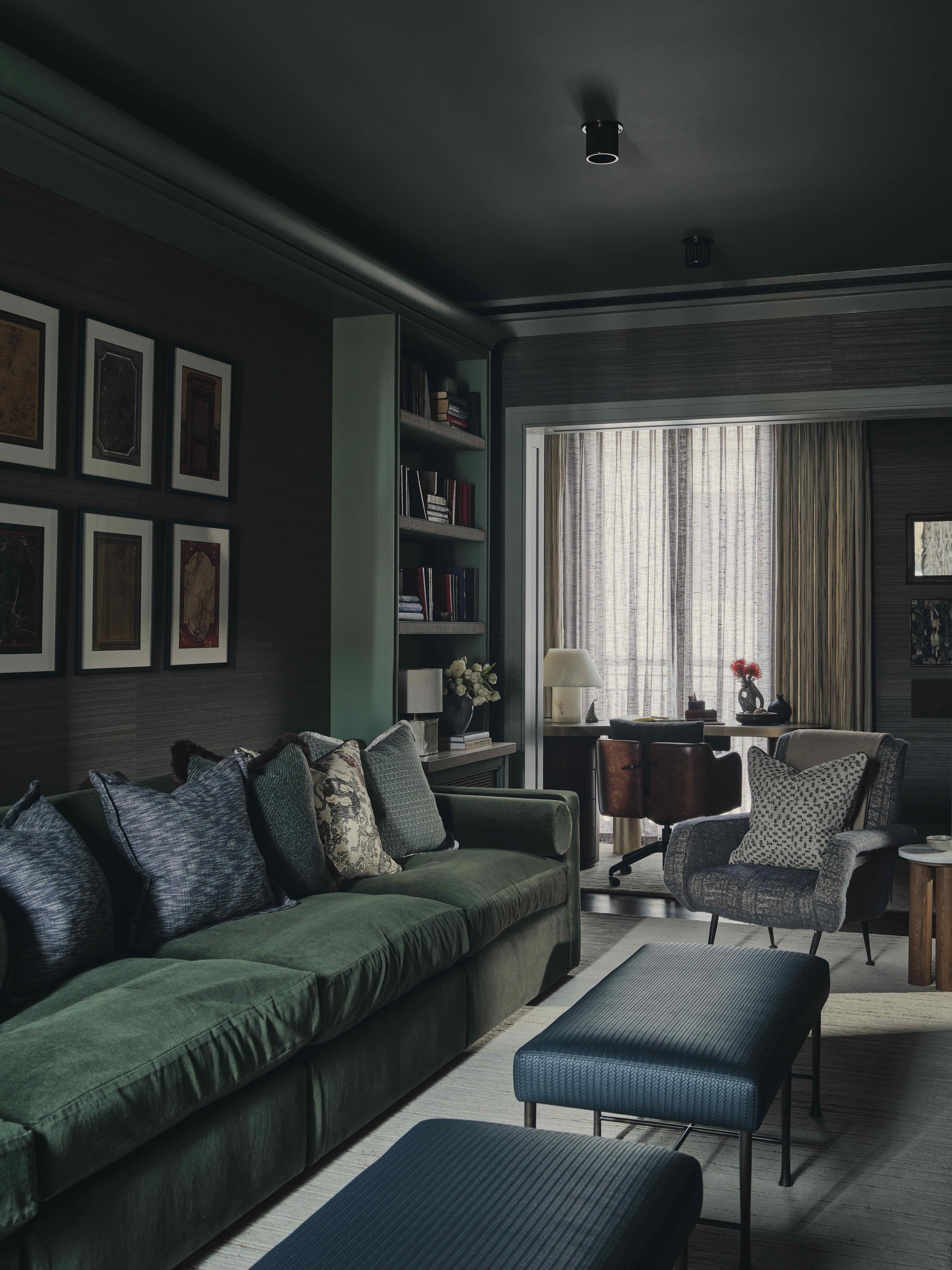 winter color palette in a modern living room, color-drenched in dark green with dark green velvet sofa, dark blue cushions and ottoman, dark-colored sheer curtains, an armchair with a patterned cushion