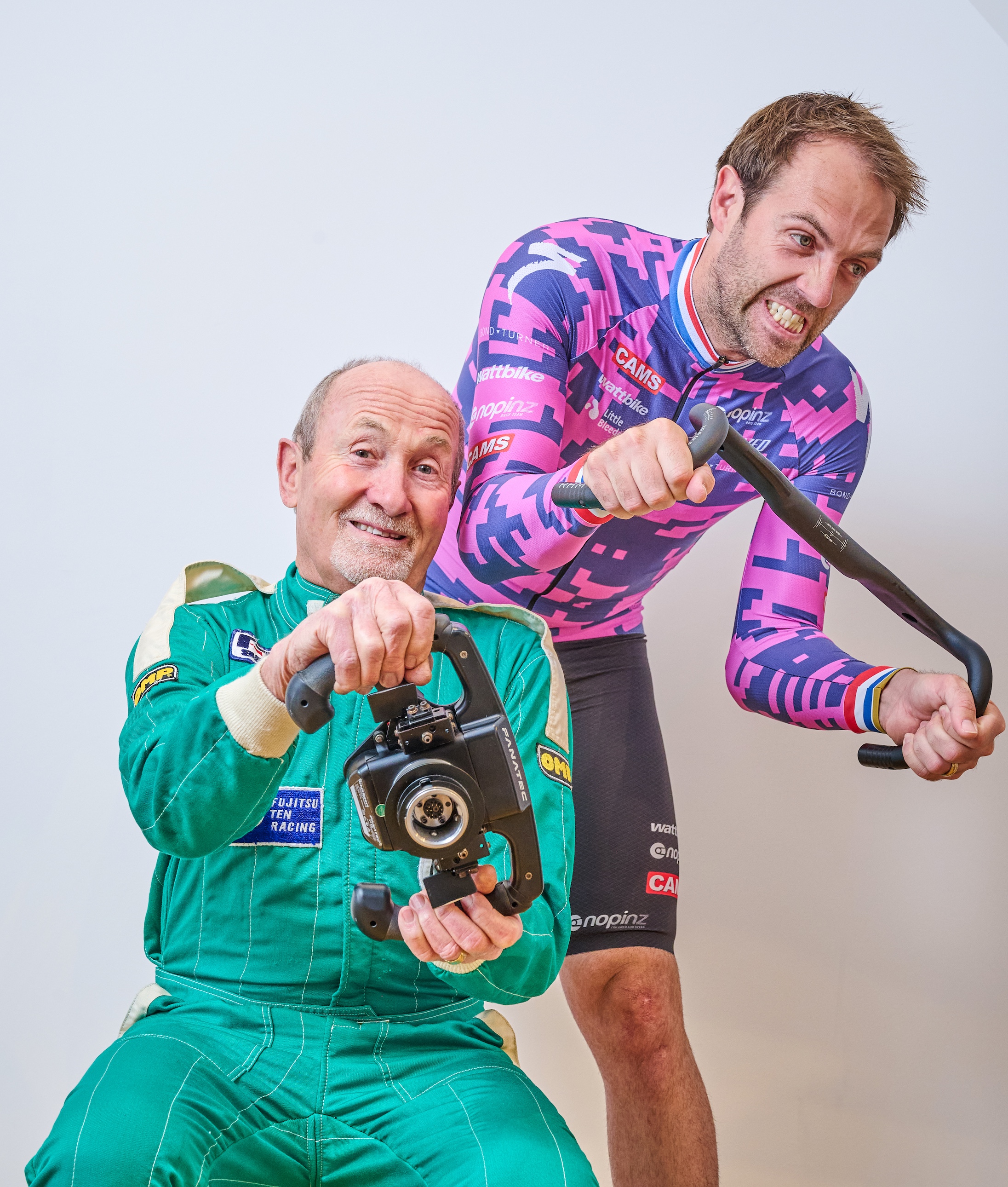 Alex Dowsett standing behind his dad, Alex holding a set of handlebars, his dad with a steering wheel