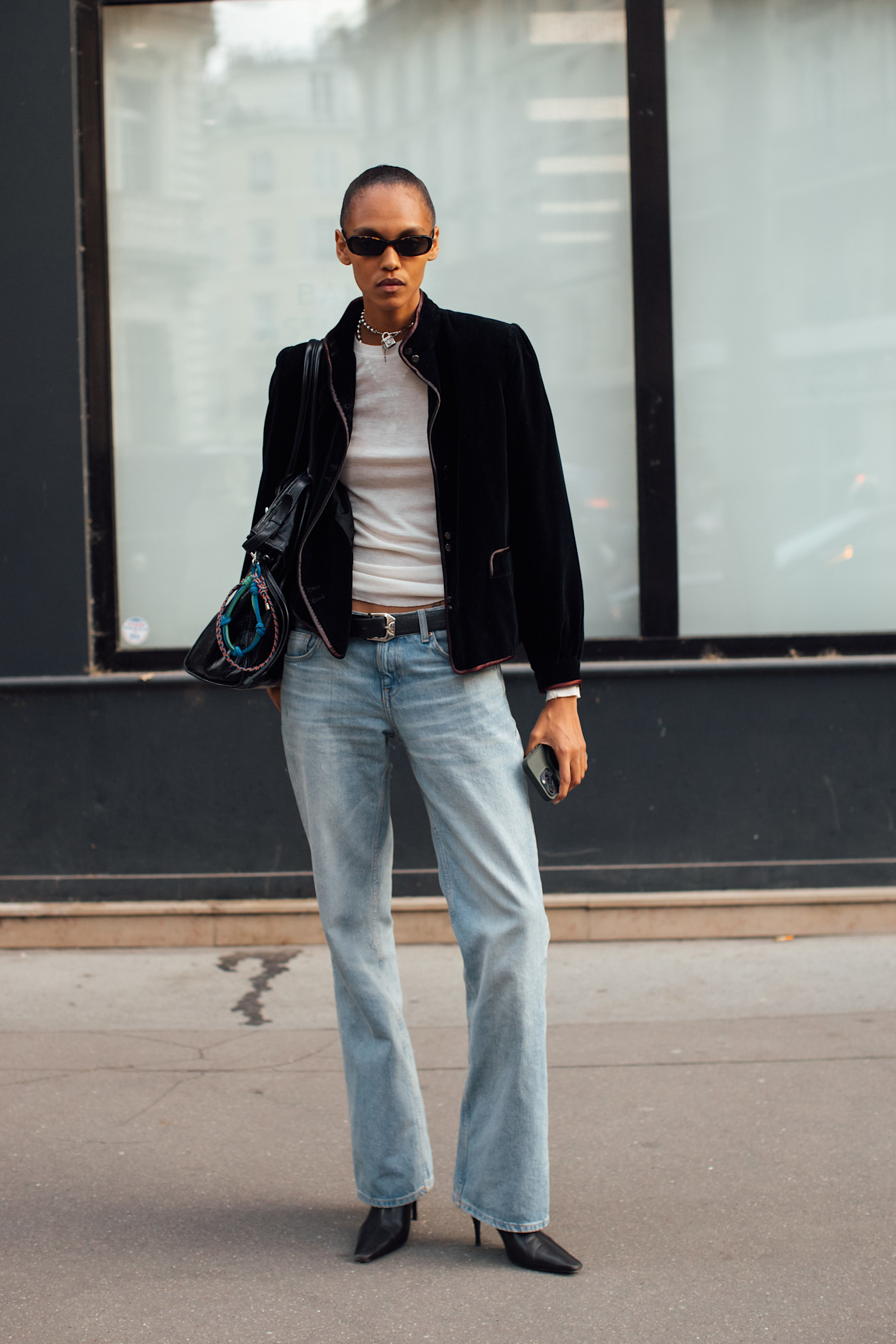 Person wearing low-rise bootcut jeans, heeled boots, a white tee, a jacket, and sunglasses.