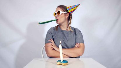 A person celebrating a birthday alone with a lone candle in a partly eaten donut.