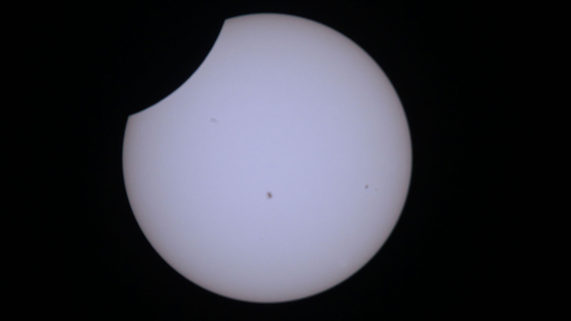 close-up view of the sun, showing the moon blocking out a top-left sliver of the solar disk