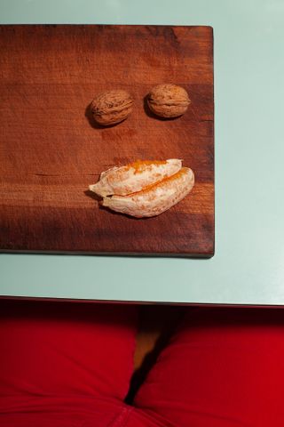 Wooden chopping board with two orange segments and two nuts on.