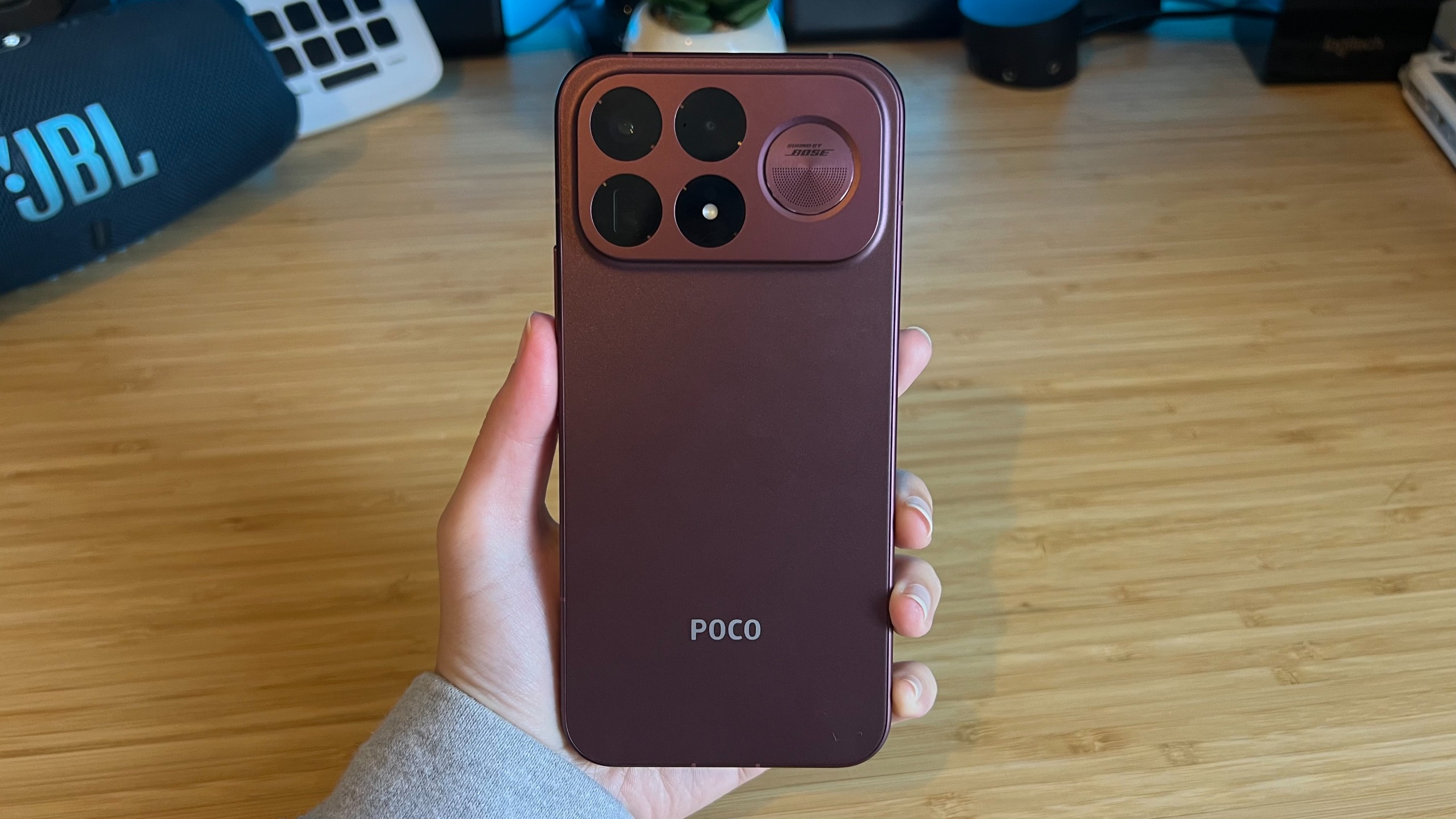 Hand holding Poco F9 Ultra smartphone over a wooden desk