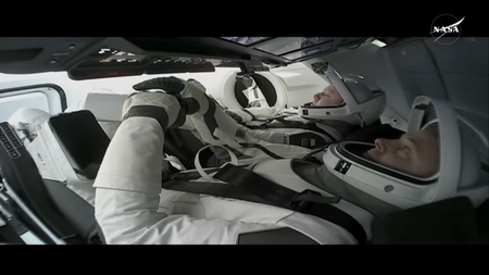 Two male astronauts inside SpaceX Dragon capsules with spacesuits on, visors up