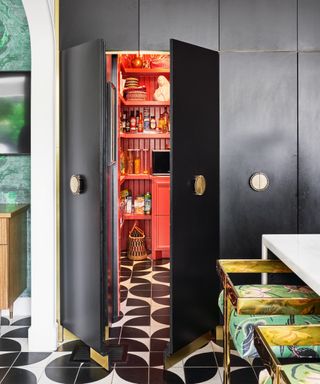 Black kitchen with red pantry, black and white flooring, metallic bar stools with fabric seats