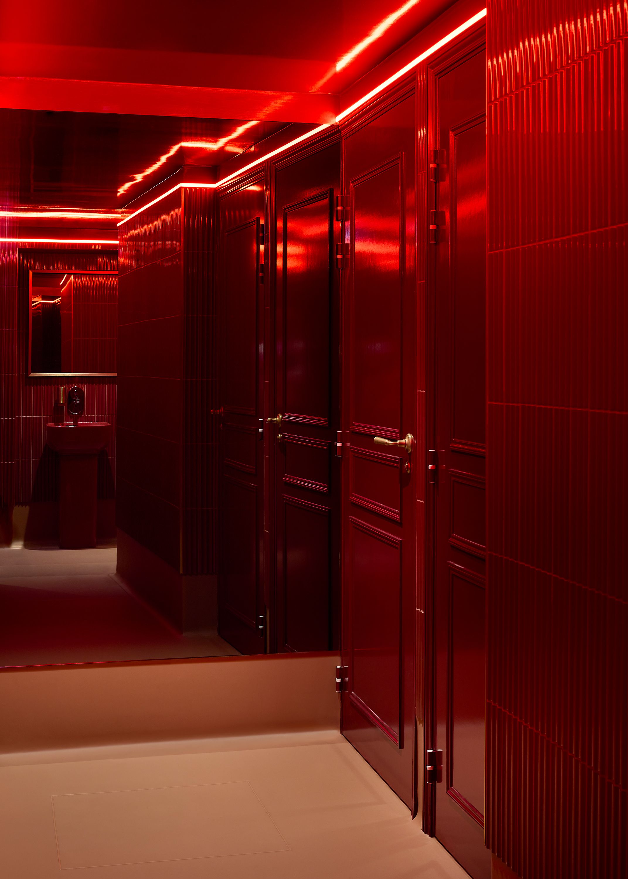 A series of interior shots depicting the retro-futuristic decor of a cinema captures velvet-clad rooms with a palette of reds, pinks, and pale dark greens, theatrical doorways, either arched or draped in curtains, ceiling porthole windows, and a vintage, golden entrance with red neon lights.