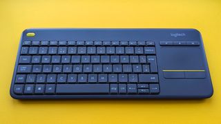 Closeup of Logitech K400 Plus wireless keyboard on a yellow background showing worn keys and buttons