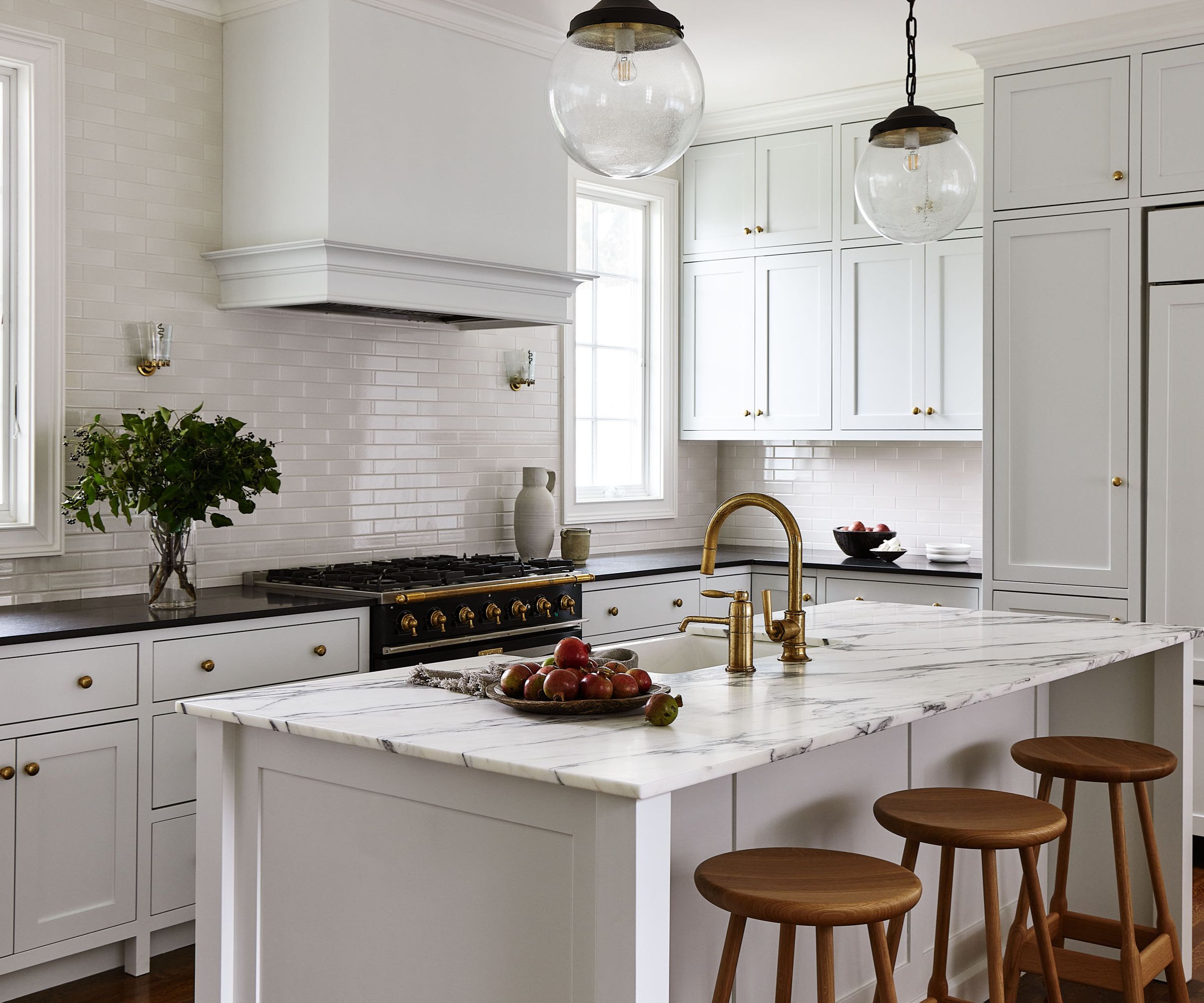 White farmhouse kitchen with white tiled backsplash, marble island and glass pendant lights