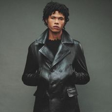 A model wearing a black leather trench coat with their hands in their pockets