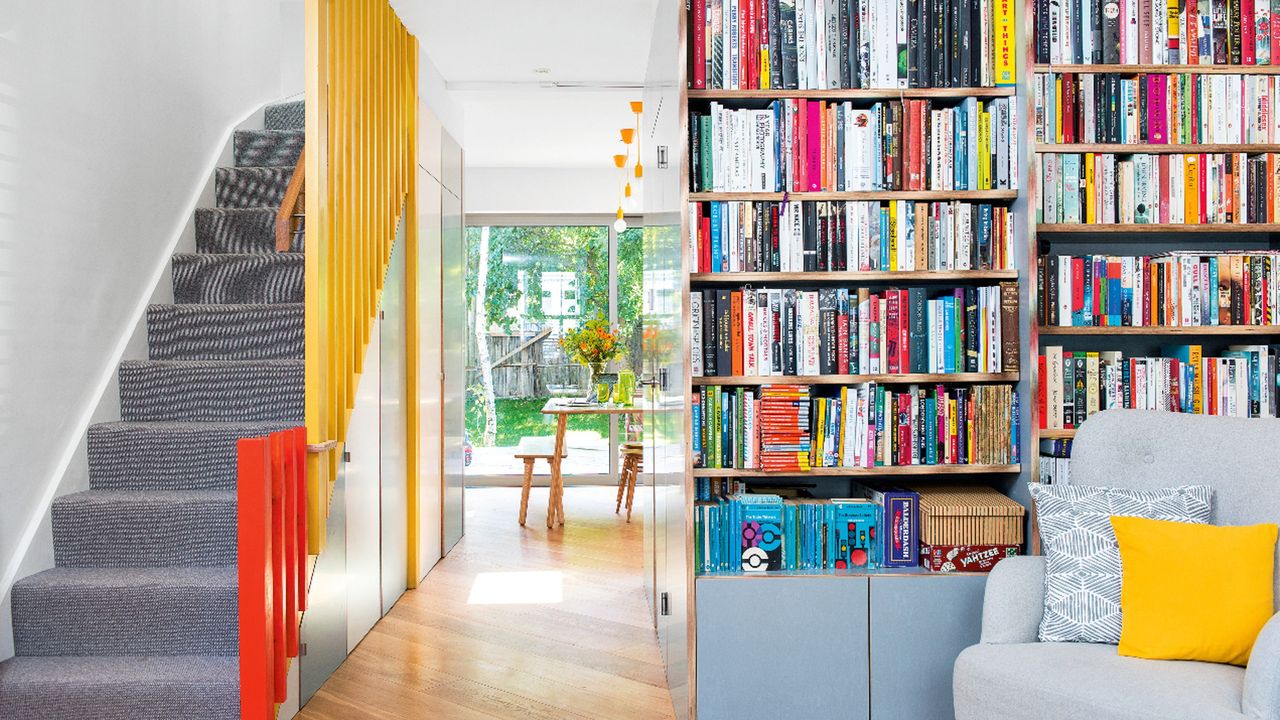 allway with storage and bookcase and doors painted in duck egg blue, with staircase opposite with grey stair carpet and yellow and orange painted banisters