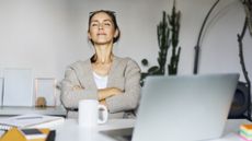 Woman sits at a desk with her eyes closed, arms folded, and a calm, satisfied look on her face