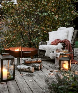 Small garden decking ideas with fire pit, candle lanterns, wicker chair and sheepskin and terracotta throws.