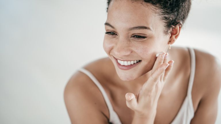 Smiling young women applying moisturiser to her face
