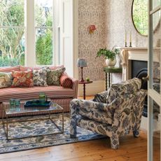 A living room with a striped red and white sofa and floral-print accent chairs matching the rug