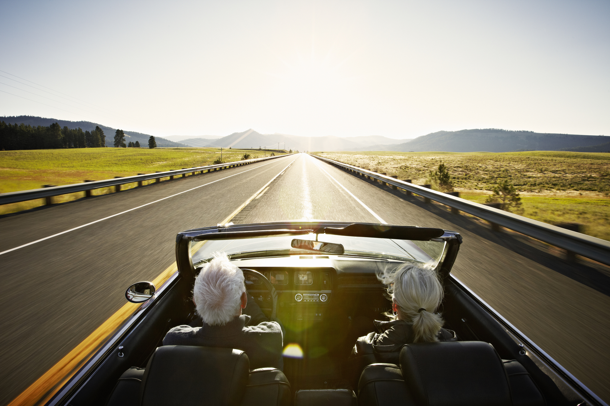A senior couple driving down an open road in a convertible.