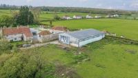 A large green building plot with an agricultural building in the middle