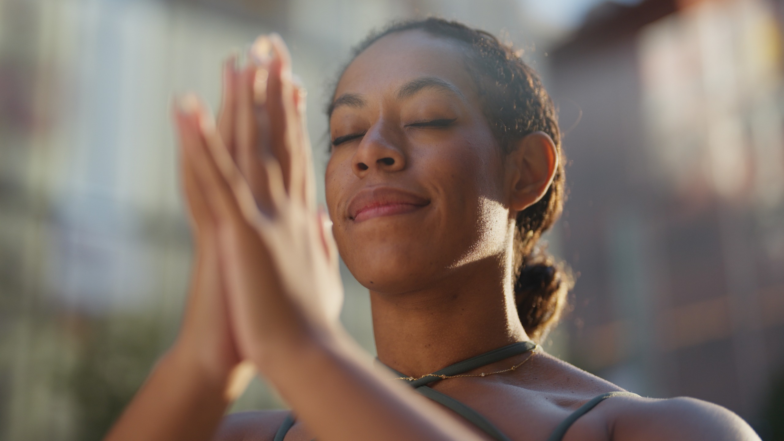 A woman stands with her eyes closed and her hands clasped together in a prayer pose. 