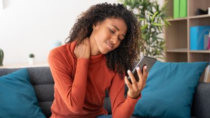 Woman scrolling phone and holding neck