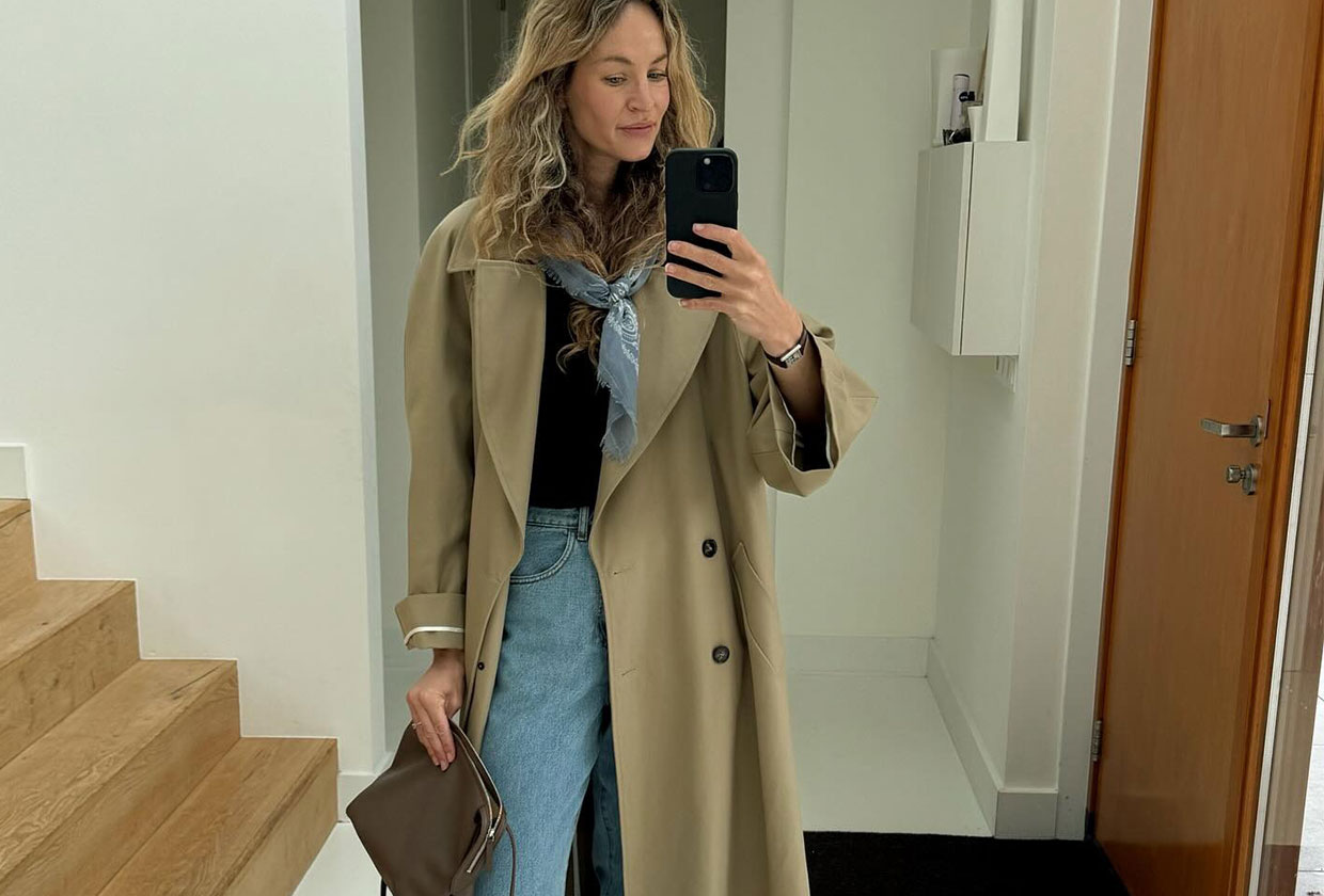 Woman wearing a tan trench coat over a black top and light wash jeans.