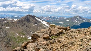 A mature mountain goat standing on a steep rocky cliff in front of Mount Bierstadt