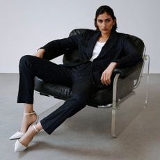 Woman wearing Saks Fifth Avenue black business suit, white tee, and white heels, sat in chair. 