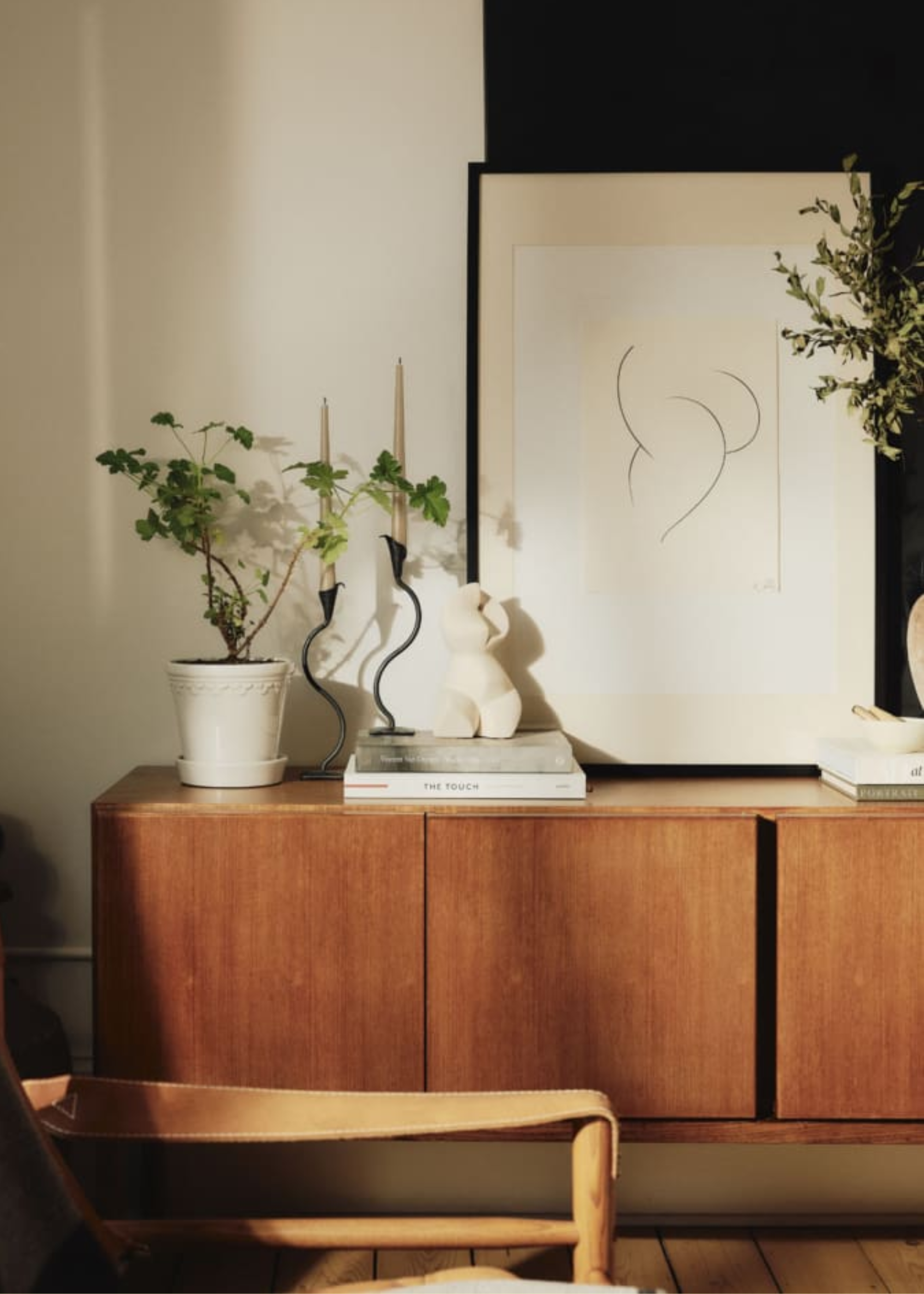 A white planter on a sideboard with a leaning painting and books