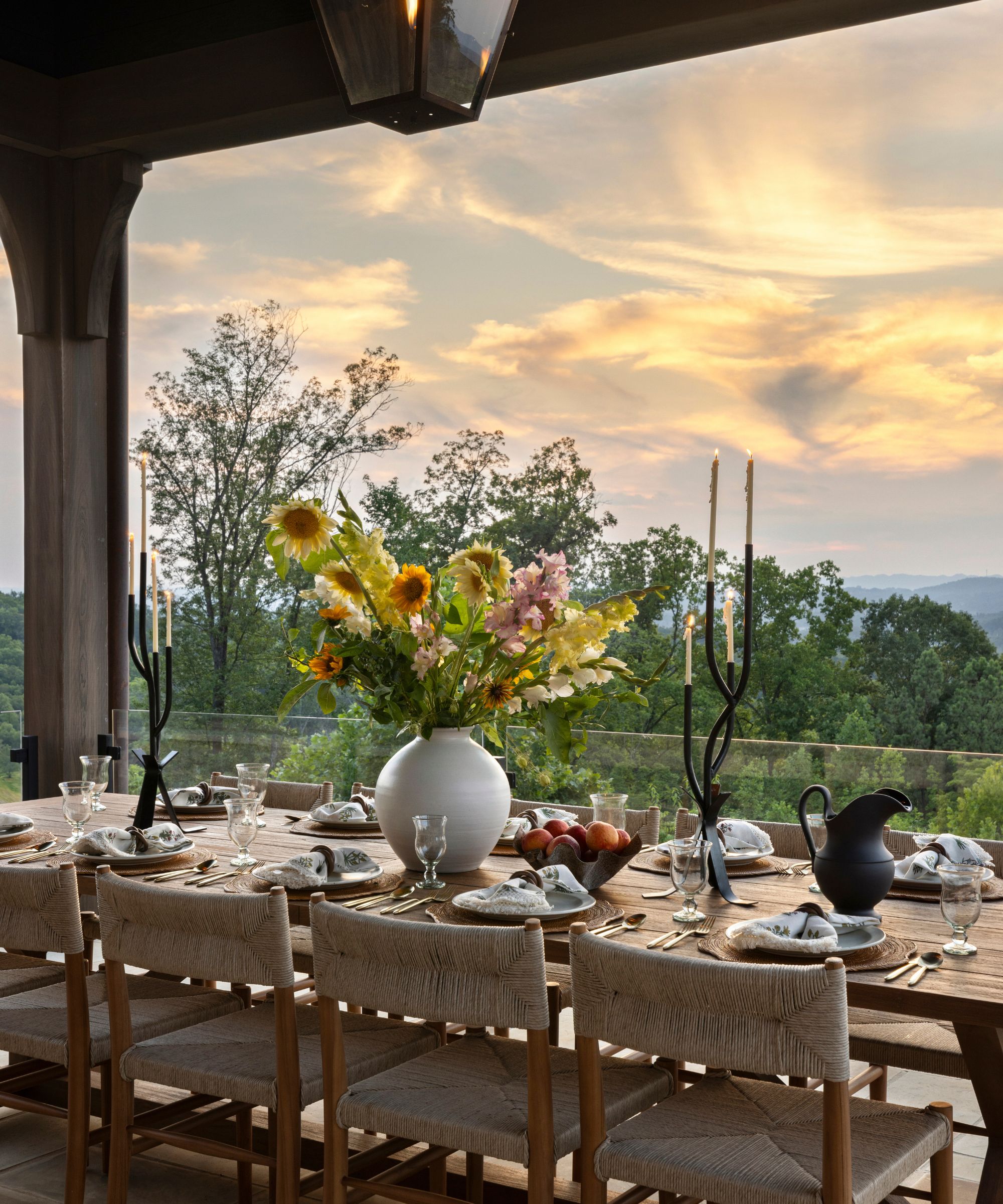 Outdoor dining table under a pergola with flowers on the table and sunset views beyond