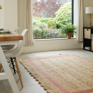 Scalloped rattan rug with pink border on living room floor by large window and desk