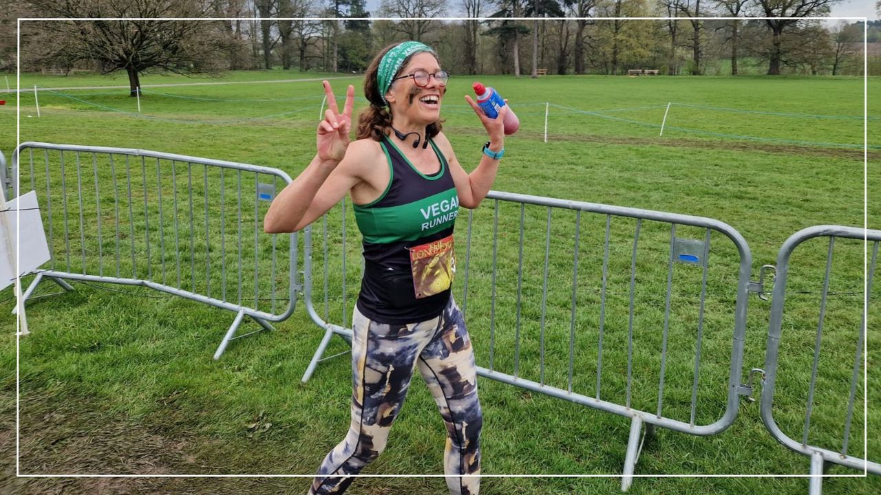 Kate Dunbar crossing the finish line of a race holding up peace signs with her fingers and holding a bottle of energy drink