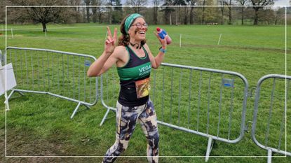 Kate Dunbar crossing the finish line of a race holding up peace signs with her fingers and holding a bottle of energy drink