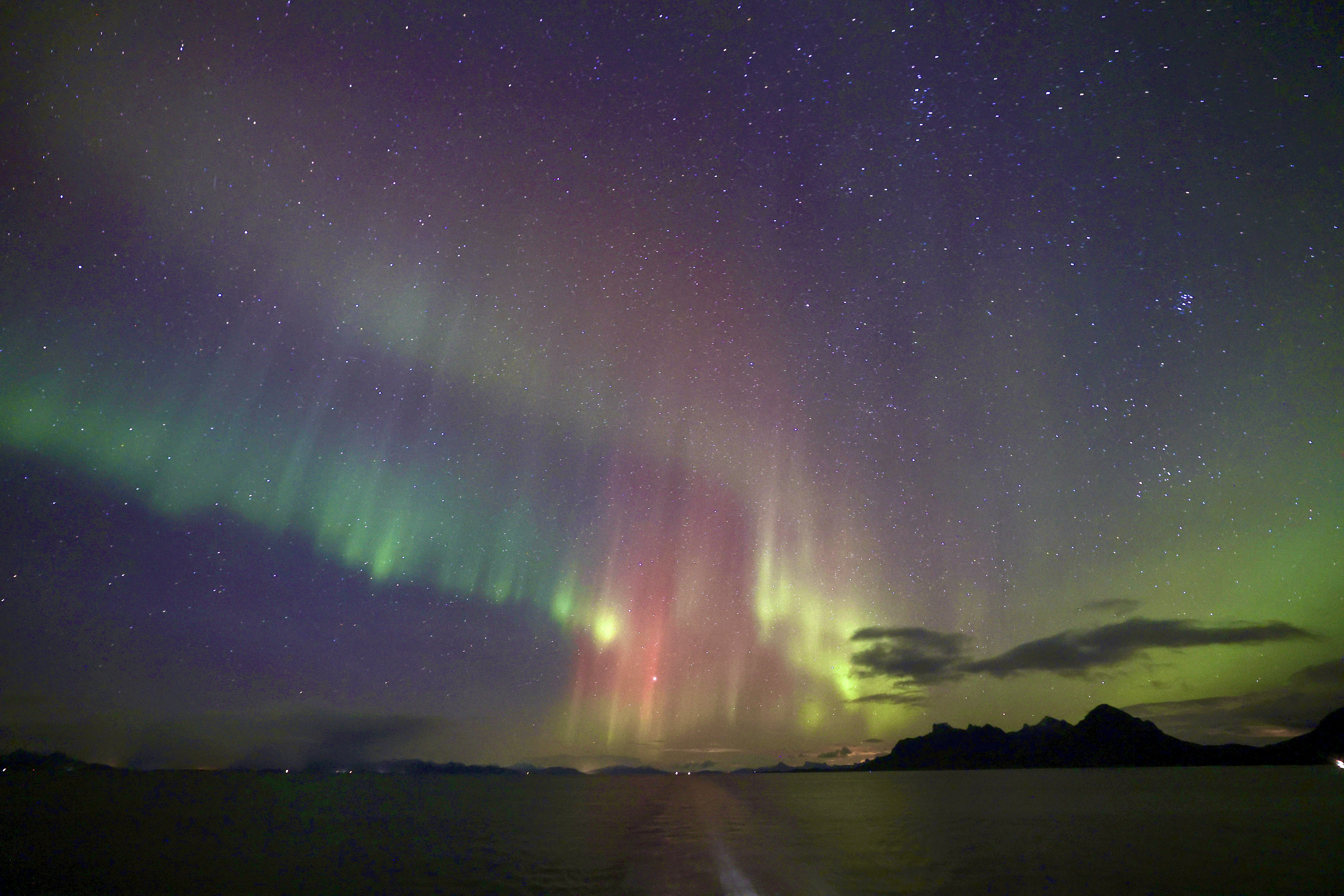 sweeping green northern lights appear as ribbons in the sky reflected in the water below